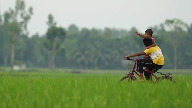 View of children riding a bicycle through rural fields Bangladesh.