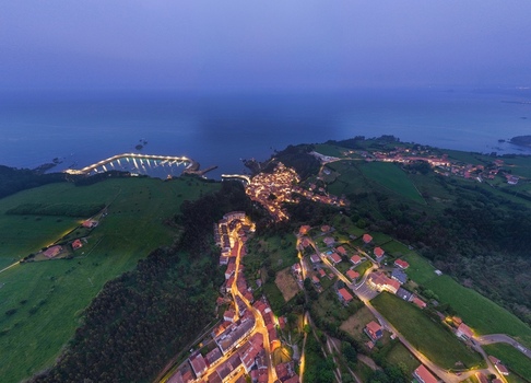 Aerial view of the illuminated coastal town of Cudillero with its harbor and surrounding green hills at twilight in Cudillero Asturias Spain. Aerial view of the illuminated coastal town of Cudillero with its harbor and surrounding green hills at twilight in Cudillero Asturias Spain.