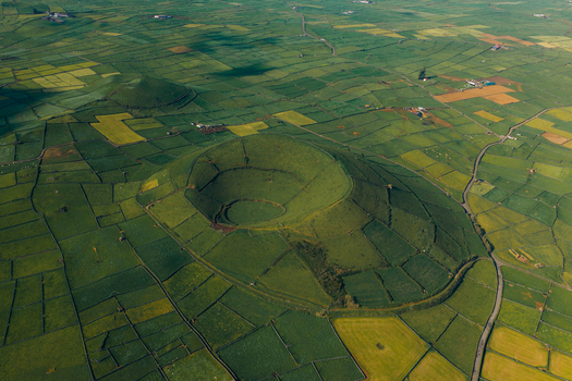 Aerial view of Pico Dona Joana volcanic crater surrounded by a patchwork of green agricultural fields and stone walls in Feteira Acores Portugal.