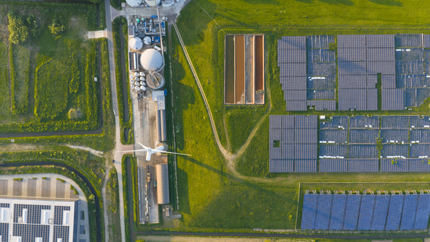 Aerial view of the Wabico BV renewable energy facility featuring solar panel arrays a wind turbine and industrial tanks surrounded by green fields in Waalwijk Noord Brabant Netherlands.