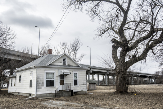View of a small white house and a large bare tree with a concrete highway overpass in the background under an overcast sky in Lincoln Nebraska United States.