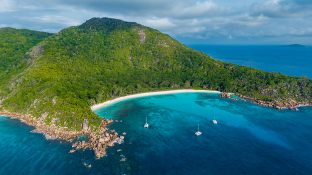 Aerial view of Anse Reunion beach with turquoise water catamarans anchored in the bay and lush green hills on the coast of Anse Reunion La Digue Seychelles.