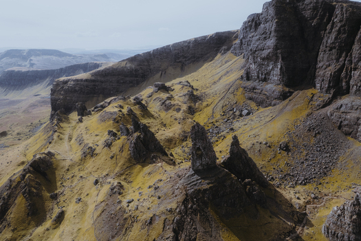 Aerial view of the dramatic rock formations and rugged basalt cliffs of The Storr with mossy green slopes and rocky terrain in Portree Scotland United Kingdom. Aerial view of the dramatic rock formations and rugged basalt cliffs of The Storr with mossy green slopes and rocky terrain in Portree Scotland United Kingdom.
