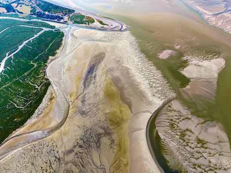 Aerial view of Baie de Somme featuring intricate tidal sand patterns winding water channels and lush green salt marshes along the coastline in Saint Valery sur Somme Hauts de France France. Aerial view of Baie de Somme featuring intricate tidal sand patterns winding water channels and lush green salt marshes along the coastline in Saint Valery sur Somme Hauts de France France.
