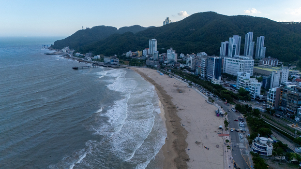 Aerial view of Songjeong Beach with sandy shoreline rolling waves coastal buildings and lush green hills in Busan Busan South Korea. Aerial view of Songjeong Beach with sandy shoreline rolling waves coastal buildings and lush green hills in Busan Busan South Korea.