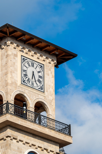View of the historic stone clock tower featuring a Roman numeral face and wrought iron balcony against a blue sky in Kruje Durres County Albania.