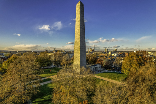Aerial view of the Bunker Hill Monument rising above a park with fall foliage contrasted against the distant city skyline Boston Massachusetts United States.