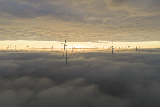 Aerial view of wind turbines emerging from a thick layer of clouds under a golden sunrise sky Netherlands. Aerial view of wind turbines emerging from a thick layer of clouds under a golden sunrise sky Netherlands.