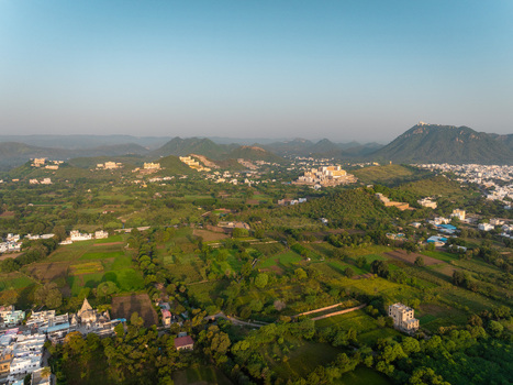 Aerial view of the lush green landscape surrounding the city of Udaipur with historic structures and rolling hills under a clear sky in Udaipur Rajasthan India.