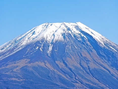 Aerial view of Mount Fuji with its snow capped peak and rugged volcanic slopes under a clear blue sky in Fujinomiya Shizuoka Japan. Aerial view of Mount Fuji with its snow capped peak and rugged volcanic slopes under a clear blue sky in Fujinomiya Shizuoka Japan.