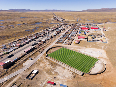 Aerial view of the town of Imata featuring a vibrant green soccer field surrounding residential buildings and a long road stretching through the arid landscape in Imata Arequipa Peru. Aerial view of the town of Imata featuring a vibrant green soccer field surrounding residential buildings and a long road stretching through the arid landscape in Imata Arequipa Peru.