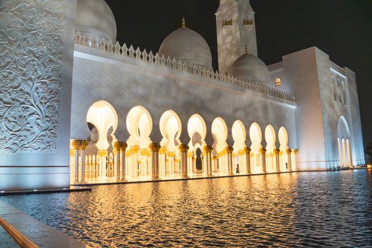 View of the illuminated Sheikh Zayed Grand Mosque with its white marble arches and domes reflected in the water at night in Abu Dhabi Abu Dhabi United Arab Emirates. View of the illuminated Sheikh Zayed Grand Mosque with its white marble arches and domes reflected in the water at night in Abu Dhabi Abu Dhabi United Arab Emirates.
