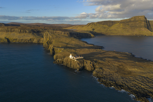 Aerial view of Neist Point Lighthouse on the edge of dramatic rocky cliffs surrounded by the deep blue sea at sunset Isle of Skye Scotland United Kingdom. Aerial view of Neist Point Lighthouse on the edge of dramatic rocky cliffs surrounded by the deep blue sea at sunset Isle of Skye Scotland United Kingdom.