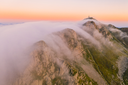 Aerial view of a mountain peak with a communication tower partially shrouded in thick clouds under a pink sunset sky Cerreto Laghi Emilia Romagna Italy. Aerial view of a mountain peak with a communication tower partially shrouded in thick clouds under a pink sunset sky Cerreto Laghi Emilia Romagna Italy.