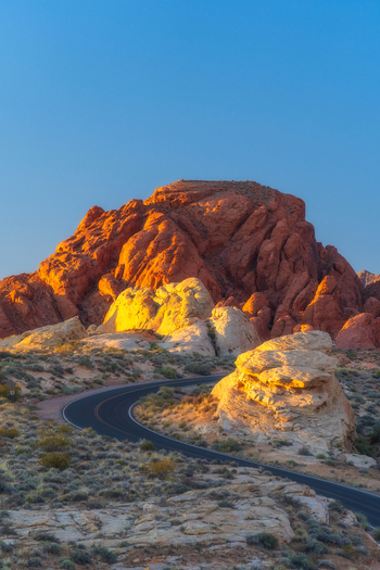 View of the winding road through red sandstone formations at Valley of Fire State Park during golden hour in Moapa Valley Nevada United States. View of the winding road through red sandstone formations at Valley of Fire State Park during golden hour in Moapa Valley Nevada United States.