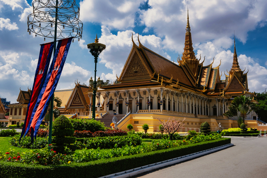 View of the Royal Palace of Cambodia featuring traditional Khmer architecture with golden roofs manicured gardens and Cambodian flags under a blue sky in Phnom Penh Phnom Penh Cambodia. View of the Royal Palace of Cambodia featuring traditional Khmer architecture with golden roofs manicured gardens and Cambodian flags under a blue sky in Phnom Penh Phnom Penh Cambodia.
