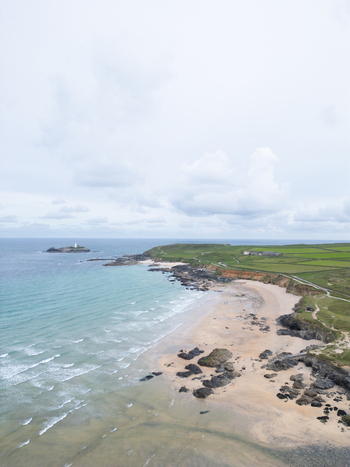 Aerial view of Godrevy Beach with turquoise waves crashing on the sand rocky cliffs and the Godrevy Lighthouse in the distance Gwithian England United Kingdom. Aerial view of Godrevy Beach with turquoise waves crashing on the sand rocky cliffs and the Godrevy Lighthouse in the distance Gwithian England United Kingdom.