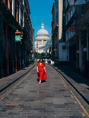 View of a woman in a vibrant red dress walking on a historic cobbled street towards the majestic dome of St. Paul s Cathedral under a clear blue sky London England United Kingdom. View of a woman in a vibrant red dress walking on a historic cobbled street towards the majestic dome of St. Paul s Cathedral under a clear blue sky London England United Kingdom.