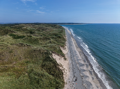 Aerial view of the coastline near Newcastle with rolling green sand dunes a long pebble beach and the blue sea under a clear sky in Newcastle Northern Ireland United Kingdom. Aerial view of the coastline near Newcastle with rolling green sand dunes a long pebble beach and the blue sea under a clear sky in Newcastle Northern Ireland United Kingdom.