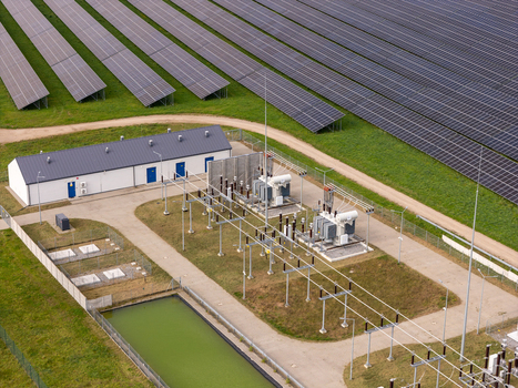 Aerial view of a solar farm with an electrical substation transformers and a small pond in Poland.
