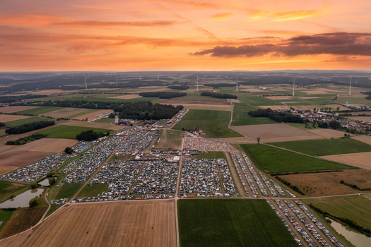 Aerial view of the Open Beatz Festival grounds with camping areas and parking lots surrounded by green fields under a sunset sky in Herzogenaurach Bayern Germany. Aerial view of the Open Beatz Festival grounds with camping areas and parking lots surrounded by green fields under a sunset sky in Herzogenaurach Bayern Germany.