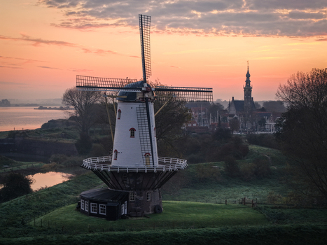 Aerial view of the historic De Koe windmill and the Grote Kerk tower under a soft sunset sky Veere Zeeland Netherlands.