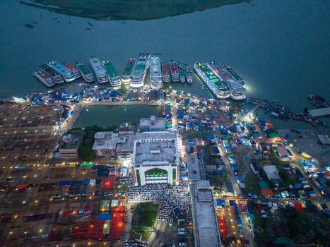Aerial view of illuminated buildings and vibrant markets sprawling along the waterfront where ferries dock under the twilight sky Charmonai Barisal Division Bangladesh. Aerial view of illuminated buildings and vibrant markets sprawling along the waterfront where ferries dock under the twilight sky Charmonai Barisal Division Bangladesh.