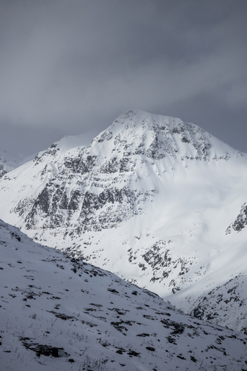 View of a majestic snow covered mountain peak under a dramatic overcast sky in the arctic wilderness of Ersfjord Troms Norway. View of a majestic snow covered mountain peak under a dramatic overcast sky in the arctic wilderness of Ersfjord Troms Norway.