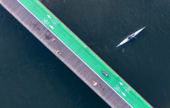 Aerial view of Tel Aviv Port featuring a green bicycle lane on a wooden bridge with pedestrians and cyclists alongside a kayak in the water in Tel Aviv Yafo Tel Aviv District Israel. Aerial view of Tel Aviv Port featuring a green bicycle lane on a wooden bridge with pedestrians and cyclists alongside a kayak in the water in Tel Aviv Yafo Tel Aviv District Israel.