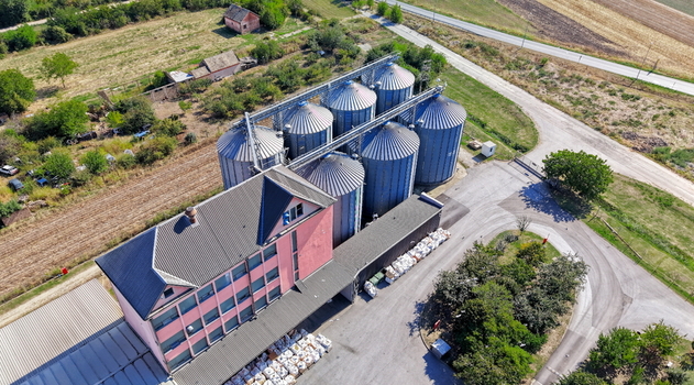 Aerial view of the storage silo Bavaniste with large metal grain bins and an adjacent pink industrial building surrounded by rural fields and roads in Bavaniste Vojvodina Serbia.
