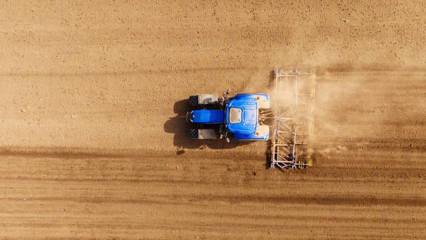 Aerial view of a blue tractor cutting through the brown earth leaving trails of disturbed soil in its wake Sremska Mitrovica Vojvodina Serbia. Aerial view of a blue tractor cutting through the brown earth leaving trails of disturbed soil in its wake Sremska Mitrovica Vojvodina Serbia.