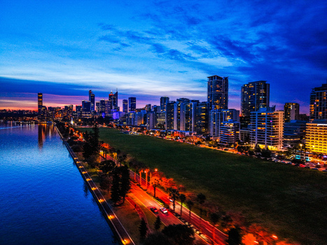 Aerial view of the Perth skyline at twilight with illuminated skyscrapers reflecting on the Swan River green parkland and city lights in City of Perth Western Australia Australia.