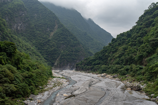 View of Taroko National Park featuring a wide rocky riverbed winding through lush green mountains under a cloudy sky in Xiulin Township Hualien County Taiwan.