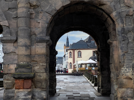 View of the ancient Roman stone archway of the Porta Nigra framing a historic street scene with buildings and a church tower in the background in Trier Rheinland Pfalz Germany.