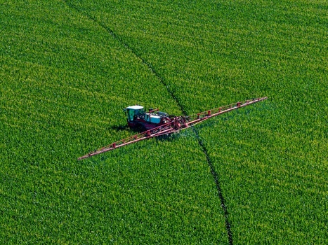 Aerial view of a tractor with a long sprayer boom working in a large green agricultural field in Hombourg Grand Est France. Aerial view of a tractor with a long sprayer boom working in a large green agricultural field in Hombourg Grand Est France.