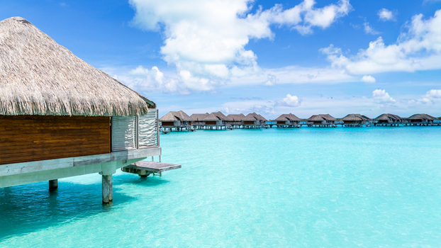 View of overwater bungalows with thatched roofs situated over the turquoise lagoon in Bora Bora Leeward Islands French Polynesia.