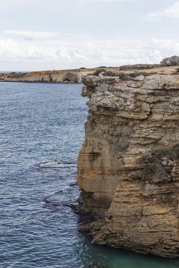 View of high limestone cliffs overlooking the turquoise Mediterranean sea under a cloudy sky Syracuse Sicily Italy.