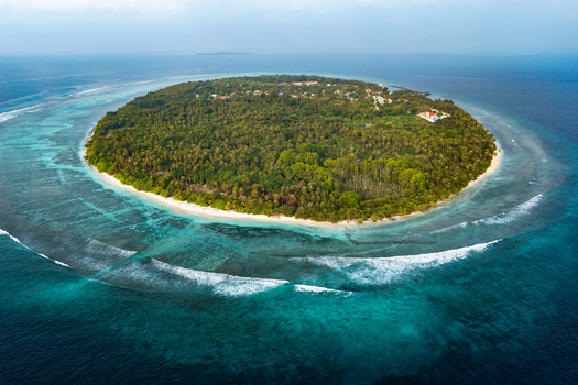 Aerial view of a lush tropical island with dense palm forests white sandy beaches and a vibrant coral reef in Vaikaradhoo Haa Dhaalu Atoll Maldives. Aerial view of a lush tropical island with dense palm forests white sandy beaches and a vibrant coral reef in Vaikaradhoo Haa Dhaalu Atoll Maldives.