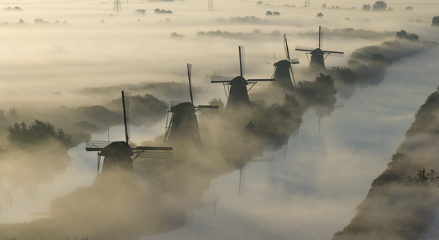 Aerial view of Unesco World Heritage Kinderdijk windmills emerging from thick morning fog along the canal Kinderdijk Zuid Holland Netherlands.