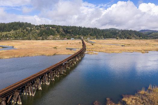 Aerial view of the Coos Bay Rail Line running through coastal wetlands near Florence Oregon showing man made rail tracks alongside marsh habitat and tidal channels.