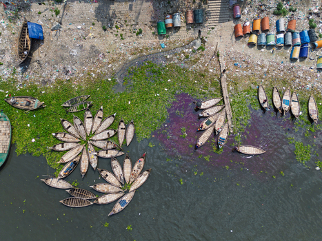 Aerial view of wooden boats arranged in flower patterns on the Buriganga River with water hyacinths and colorful barrels on the shore in Dhaka Dhaka Division Bangladesh.