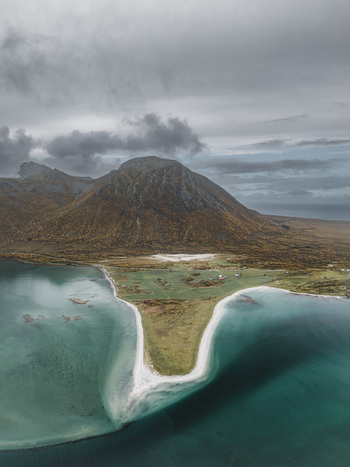 Aerial view of Lofoten landscape featuring a triangular sandy beach turquoise coastal waters and rugged mountains covered in autumn foliage in Svolvaer Nordland Norway.