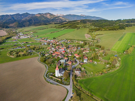 Aerial view of the historic church and village houses nestled among rolling green fields and distant mountains in Liptovske Matiasovce Zilina Region Slovakia.