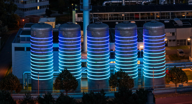Aerial view of the BTB Heat and Power Plant Adlershof at night featuring large industrial tanks illuminated with glowing blue LED rings in Berlin Berlin Germany. Aerial view of the BTB Heat and Power Plant Adlershof at night featuring large industrial tanks illuminated with glowing blue LED rings in Berlin Berlin Germany.
