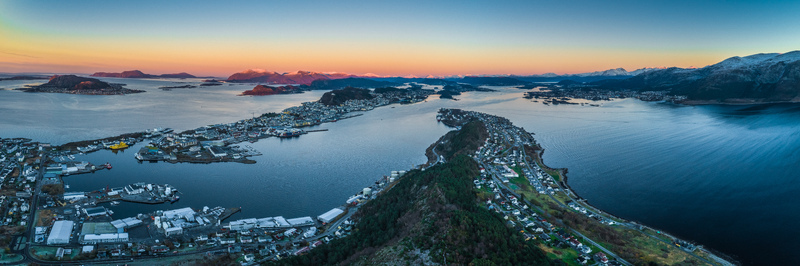 Aerial view of the coastal town of Alesund featuring its unique architecture surrounding fjords and snow capped mountains under a golden sunset sky Alesund More og Romsdal Norway. Aerial view of the coastal town of Alesund featuring its unique architecture surrounding fjords and snow capped mountains under a golden sunset sky Alesund More og Romsdal Norway.