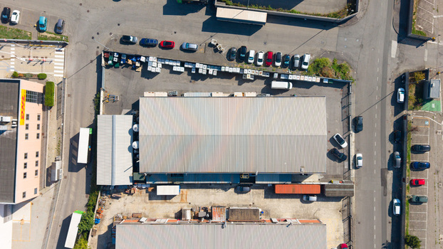 Aerial view of an industrial facility with a large warehouse building surrounding parking lots filled with cars and asphalt surfaces in Milan Lombardy Italy.
