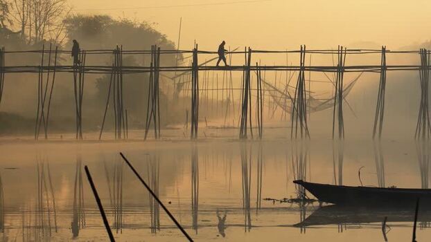 View of people on a bamboo bridge over a misty river Bangladesh.