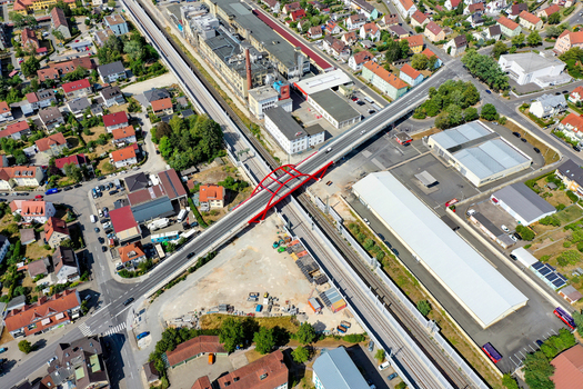 Aerial view of Piastenbrucke red bridge crossing over railway tracks surrounded by industrial buildings and residential houses in Forchheim Bayern Germany.