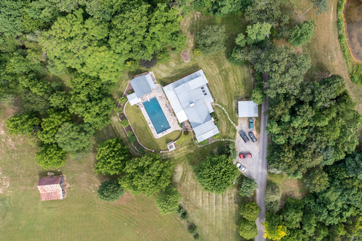 Harrisonburg United States 09 August 2021 Aerial view of a residential property featuring a swimming pool a metal roofed house and a gravel driveway surrounded by lush green trees and open fields. Harrisonburg United States 09 August 2021 Aerial view of a residential property featuring a swimming pool a metal roofed house and a gravel driveway surrounded by lush green trees and open fields.