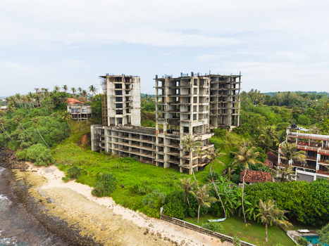 Aerial view of an unfinished concrete building skeleton on a lush tropical coastline with palm trees and ocean waves Mirissa Southern Province Sri Lanka. Aerial view of an unfinished concrete building skeleton on a lush tropical coastline with palm trees and ocean waves Mirissa Southern Province Sri Lanka.